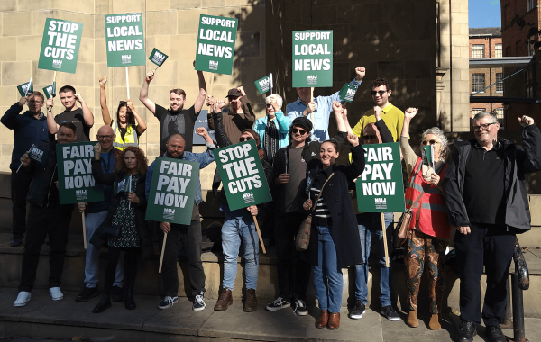 Large group of journalists holding placards saying fair pay now, stop the cuts and support local news.