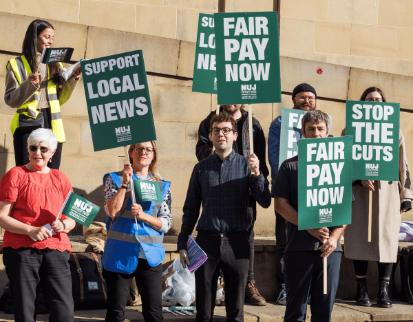 Journalists on a picket line holding greenplacards saying fair pay now, support local news