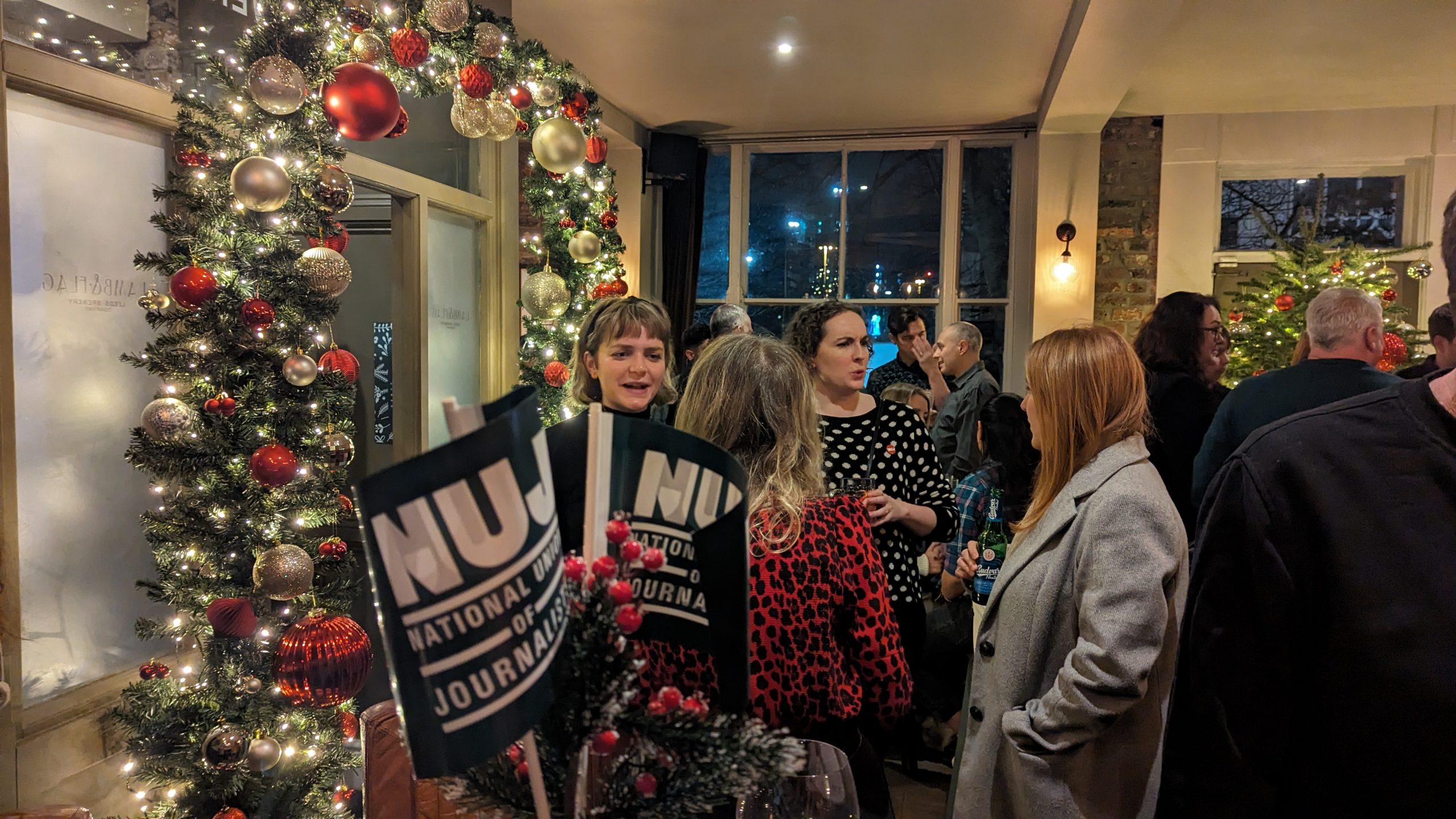 People talking in a pub with christmas decorations, and NUJ flags in the foreground.