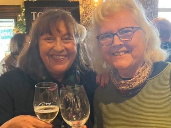 Two women smiling at the camera while each raising a glass