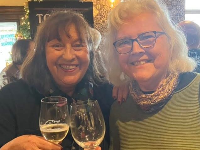 Two women smiling at the camera while each raising a glass