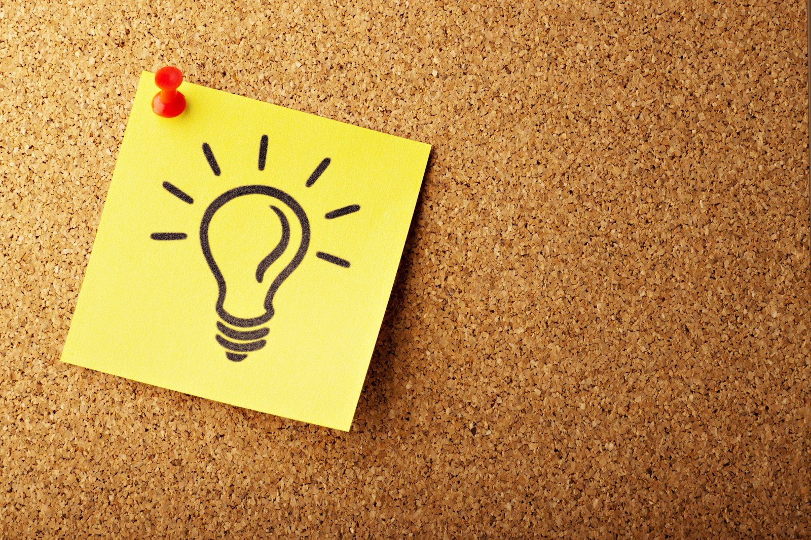A yellow post-it note with a line drawing of a lightbulb, pinned toa cork noticeboard with a red pin